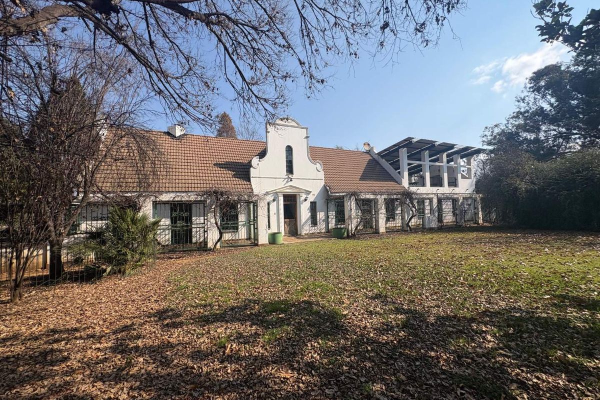 Rear view of a traditional farmhouse featuring a gabled roofline, security-fitted windows, and an attached covered patio area overlooking a large garden.