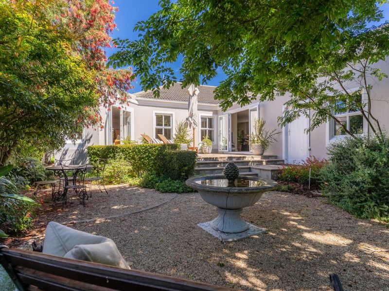 A beautifully landscaped rear courtyard featuring a central stone fountain, gravel pathways, and direct access to the home through double french doors.