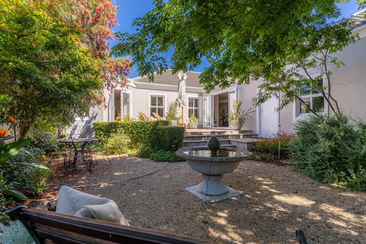 A beautifully landscaped rear courtyard featuring a central stone fountain, gravel pathways, and direct access to the home through double french doors.