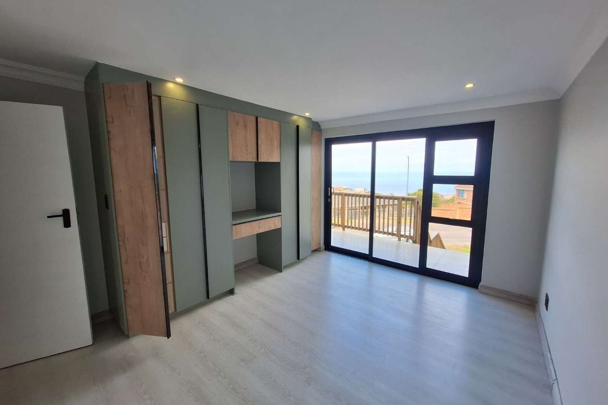 A bright bedroom featuring modern built-in cabinetry with a desk area, light wood-look flooring, and sliding glass doors leading to an outdoor balcony.