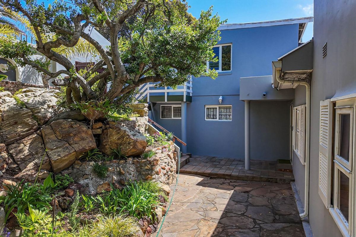 A private rear courtyard featuring natural stone paving, a landscaped rockery with mature trees, and direct access to the multi-level residential structure.