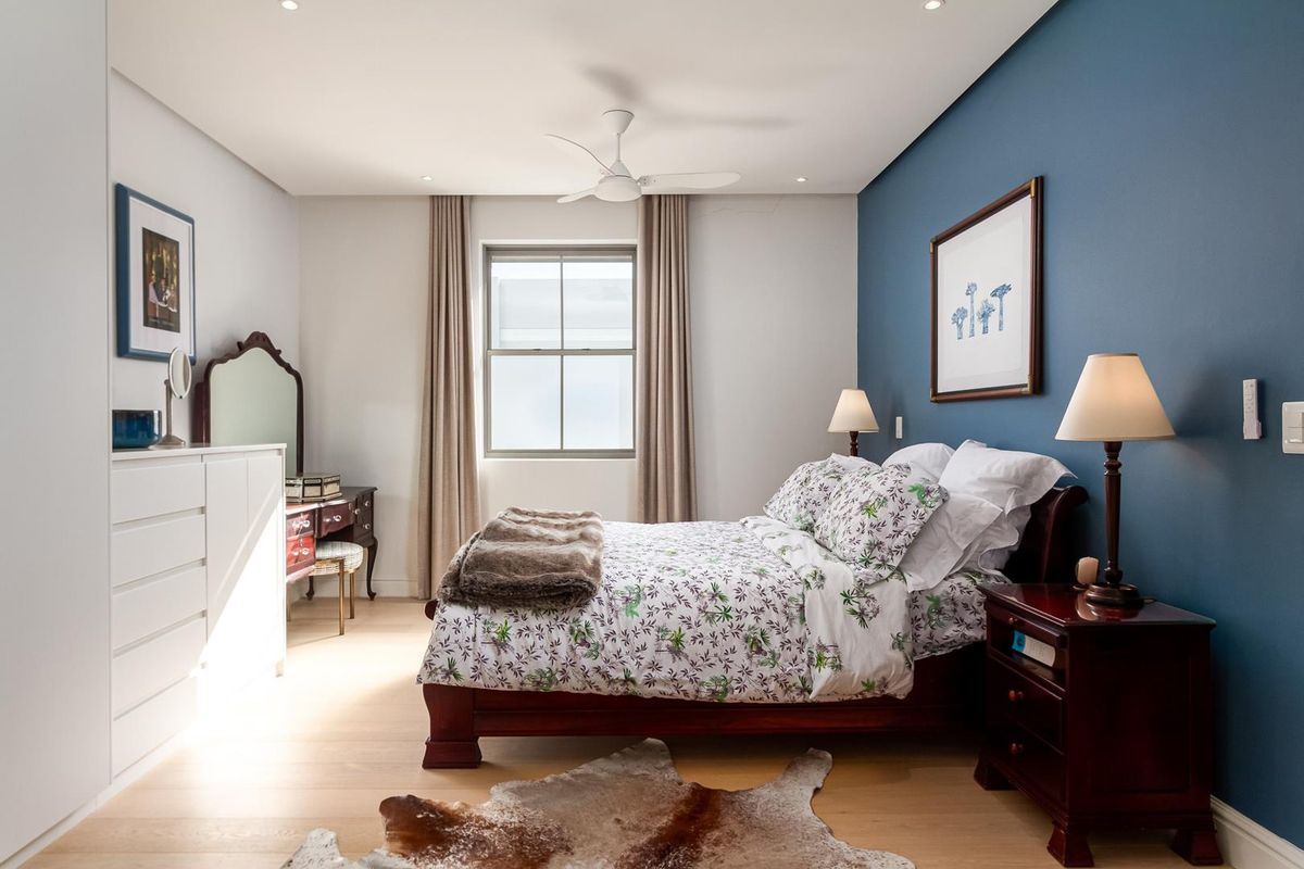A well-maintained bedroom featuring light timber flooring, a built-in wardrobe, recessed ceiling lighting, and a ceiling fan with a feature blue accent wall.