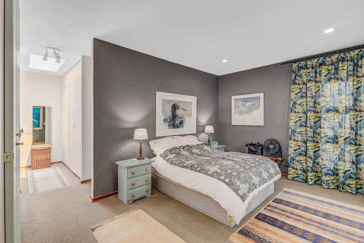 Spacious bedroom featuring a dark accent wall, recessed lighting, and an adjoining walk-through closet area with built-in storage.