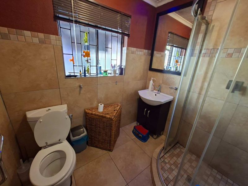 A functional bathroom featuring a shower enclosure, vanity cabinet with basin, toilet, and neutral wall tiling with decorative accents.