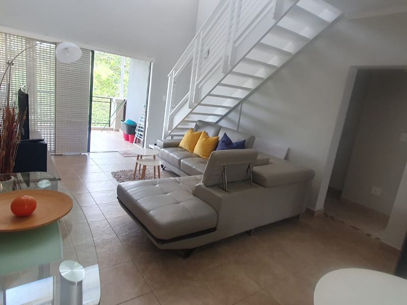 Open plan living area featuring tiled flooring, a modern staircase, and direct access to a private balcony through sliding glass doors.
