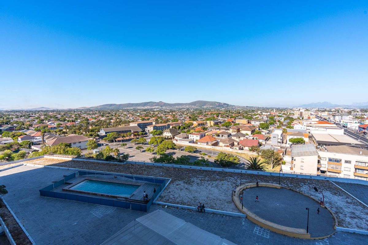 An elevated aerial view of the apartment complex rooftop featuring a swimming pool and paved recreational area, overlooking the surrounding suburban landscape.