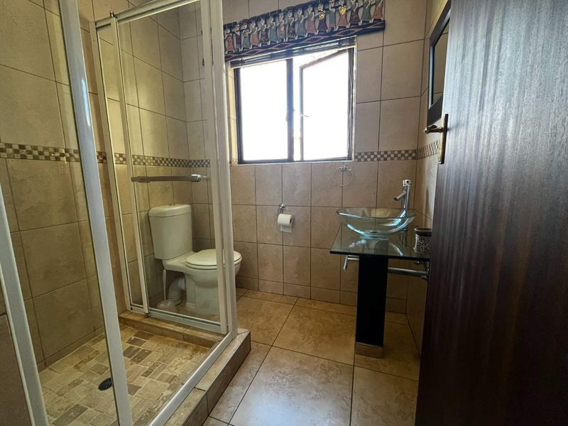 A functional bathroom featuring a glass shower enclosure, a modern glass vessel sink on a pedestal vanity, and neutral wall and floor tiling.