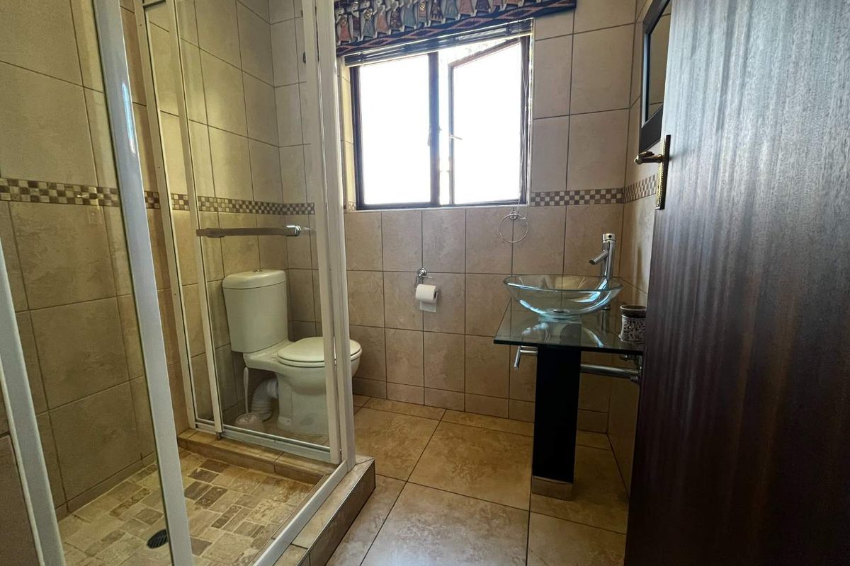 A functional bathroom featuring a glass shower enclosure, a modern glass vessel sink on a pedestal vanity, and neutral wall and floor tiling.
