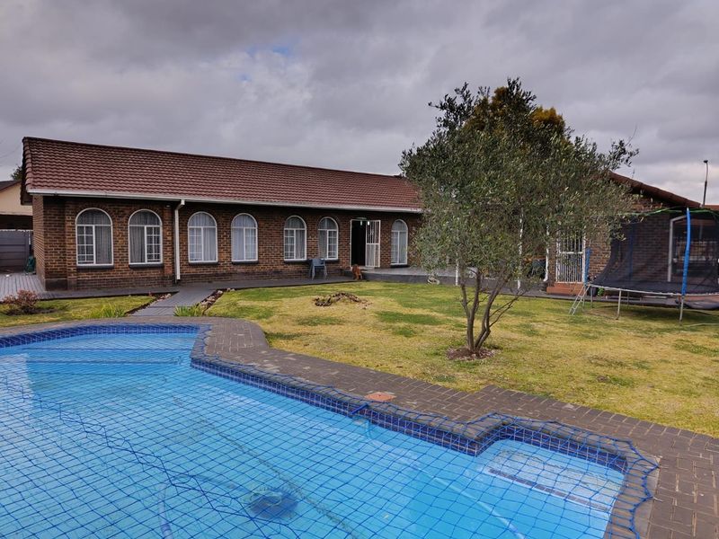 Rear view of a brick house featuring a swimming pool with safety net, paved surround, and a well-maintained lawn area.