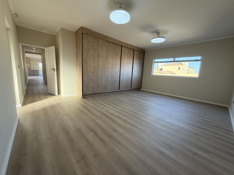 A spacious, empty bedroom featuring modern laminate flooring and large built-in wooden cupboards, offering a clean and neutral canvas.