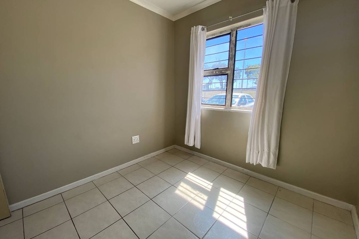 A compact, empty bedroom featuring neutral wall paint, tiled flooring, and a window fitted with security bars.