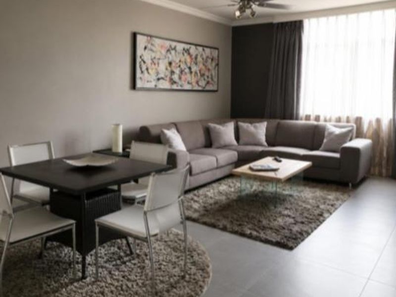 A well-maintained living room featuring neutral tiled flooring, crown molding, and a central ceiling fan, creating a comfortable and cohesive living space.