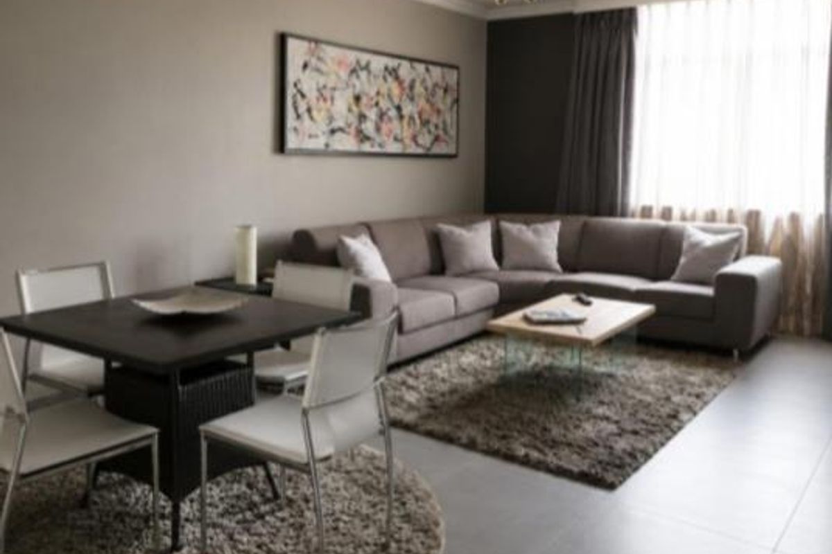 A well-maintained living room featuring neutral tiled flooring, crown molding, and a central ceiling fan, creating a comfortable and cohesive living space.
