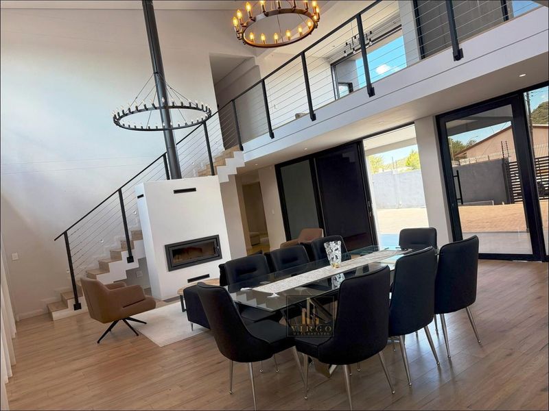 Spacious open-plan living and dining area featuring a double-volume ceiling, suspended fireplace, mezzanine level, and large sliding doors leading to the exterior.