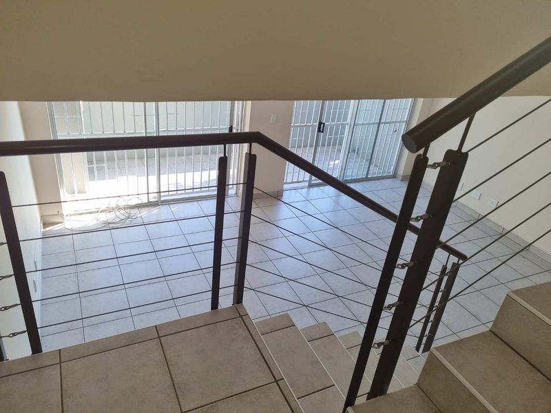 An open-plan living area viewed from the staircase, featuring tiled flooring and sliding glass doors leading to an outdoor space.