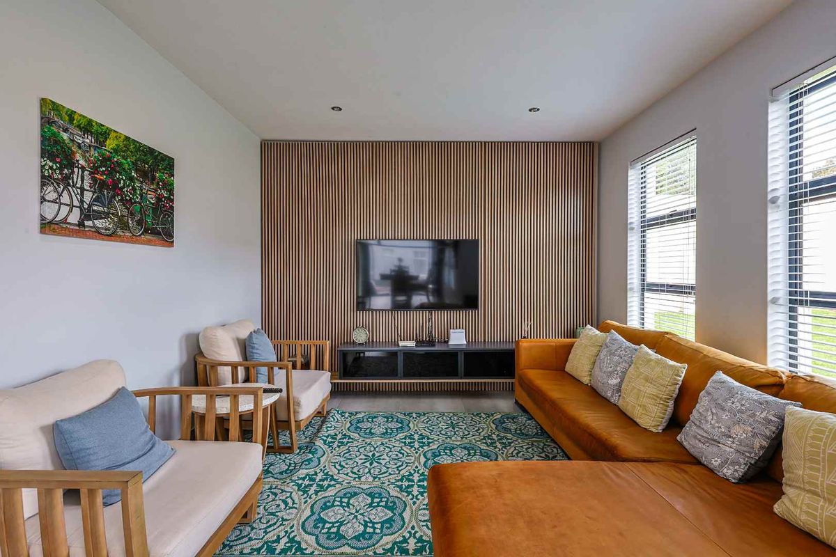 A modern living room featuring a stylish vertical timber slat feature wall, recessed downlighting, and large windows providing ample natural light.