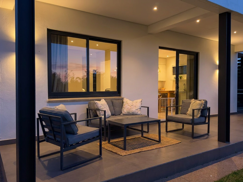 A modern covered patio featuring tiled flooring, recessed lighting, and black structural pillars, providing a seamless transition to the interior living space.