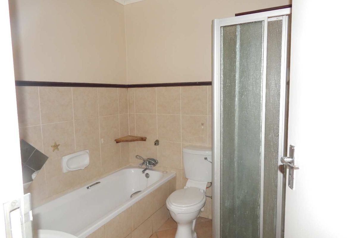 A functional bathroom featuring a built-in bathtub, separate shower enclosure, and toilet with neutral wall tiling.