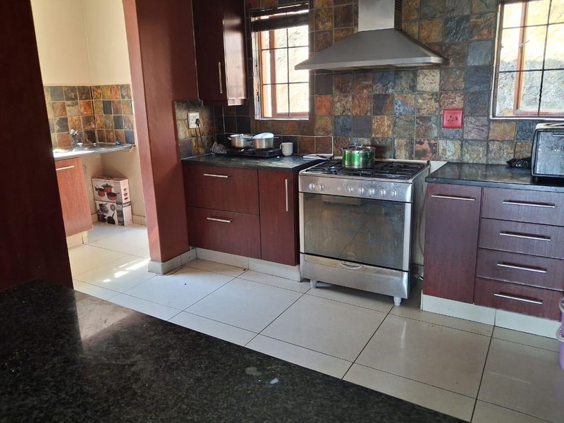 Functional kitchen featuring dark wood cabinetry, granite countertops, a stainless steel gas stove with extractor fan, and a tiled backsplash.