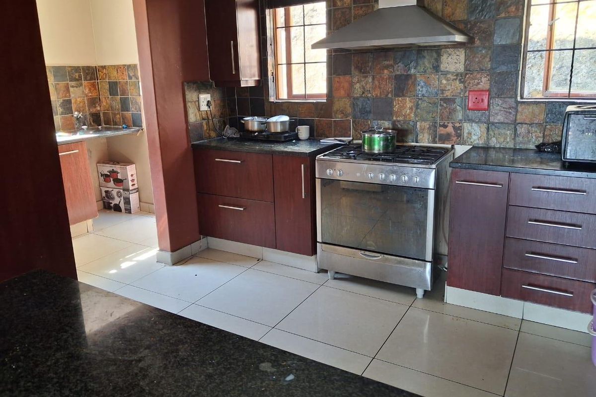 Functional kitchen featuring dark wood cabinetry, granite countertops, a stainless steel gas stove with extractor fan, and a tiled backsplash.