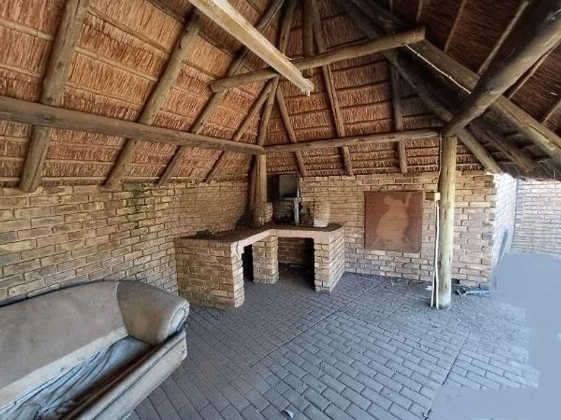 Covered outdoor patio area featuring a traditional thatched roof, exposed timber beams, and a built-in brick braai station with paved flooring.