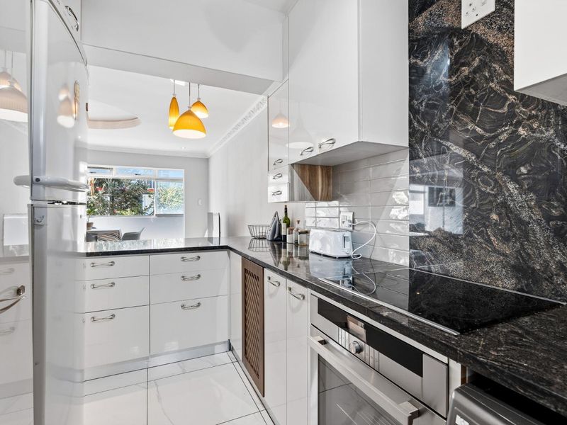 Modern kitchen featuring high-gloss white cabinetry, granite countertops, a striking stone feature splashback, and integrated electric cooking appliances.