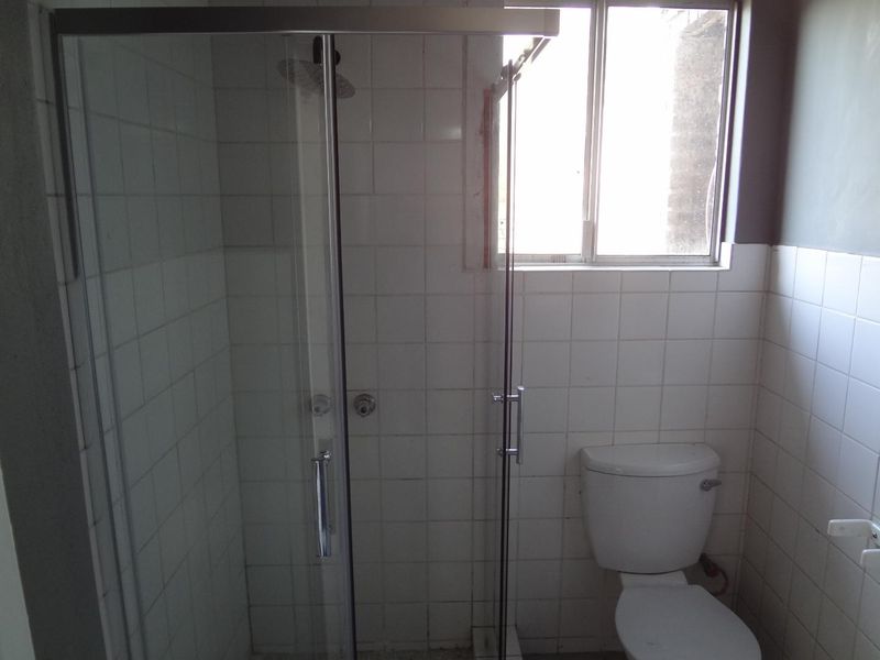 A functional bathroom featuring a glass shower enclosure, white wall tiling, and a standard toilet, requiring some cosmetic updates to the finishes.