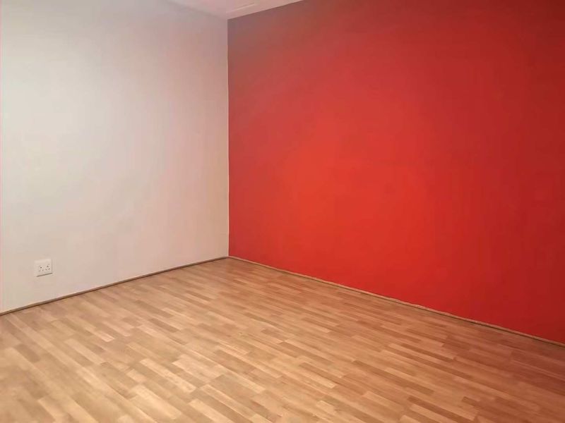 An empty room featuring laminate flooring and a bold red accent wall, providing a blank canvas for personalization.