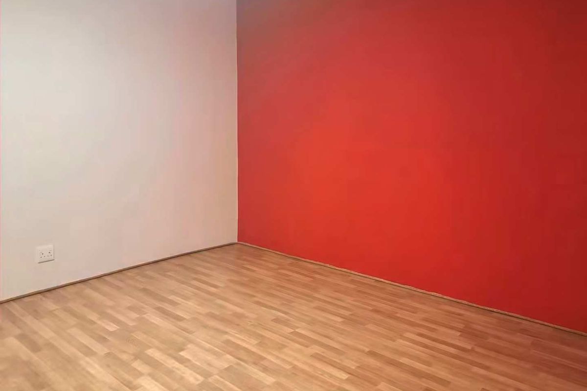 An empty room featuring laminate flooring and a bold red accent wall, providing a blank canvas for personalization.