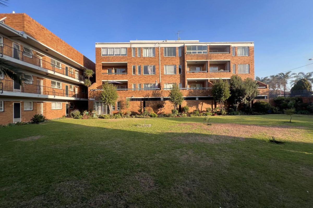 View of the rear brick apartment building facade featuring multiple balconies and a shared communal garden area.