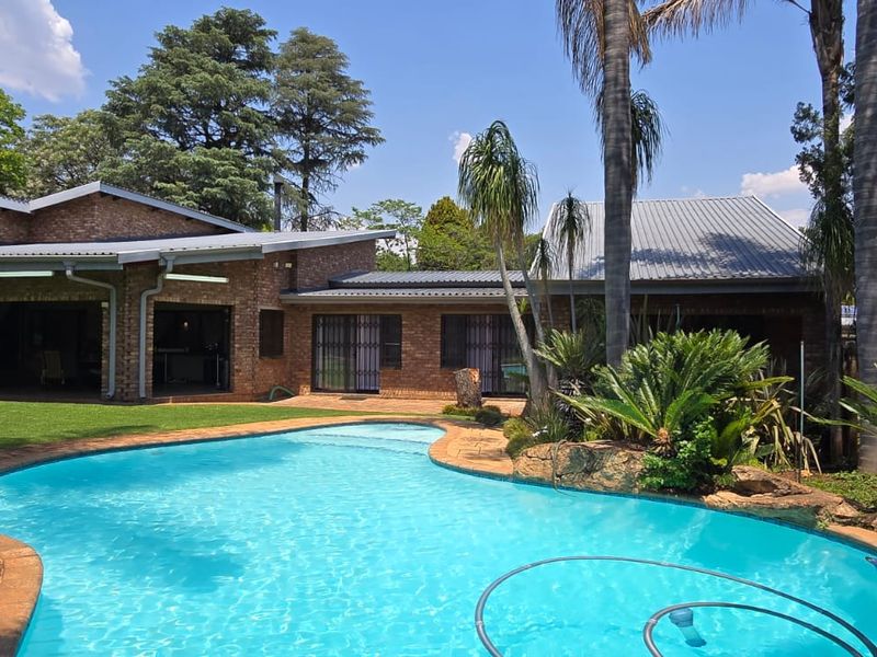 A well-maintained backyard featuring a swimming pool, established garden, and a brick-clad house with a covered patio area.