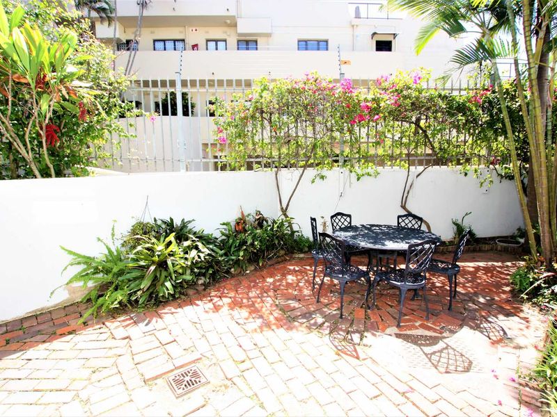 A private rear courtyard featuring brick paving, perimeter walling with security fencing, and established garden greenery.