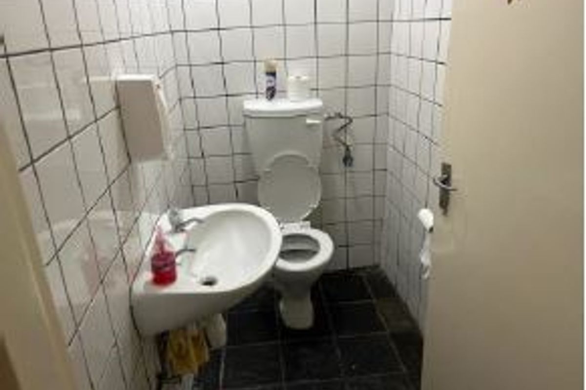 A compact office restroom featuring a wall-mounted basin and toilet with white tiled walls and dark floor tiles, requiring cosmetic updates.