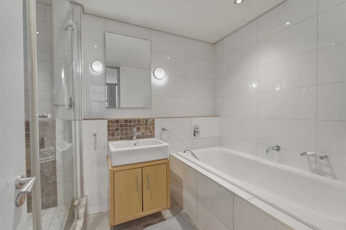 A clean, modern bathroom featuring a built-in vanity, a separate shower enclosure, and a bathtub with white wall tiling.