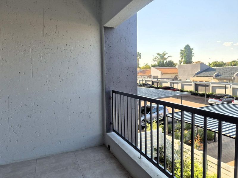 A clean, covered balcony featuring tiled flooring and a modern metal balustrade, offering an elevated view of the complex parking area.