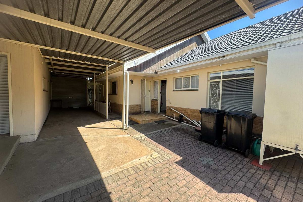 Rear exterior view featuring a covered carport, paved driveway area, and access to the main dwelling with security gates and window bars.