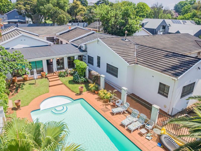 Aerial view of a residential property featuring a swimming pool, paved patio area, and a well-maintained garden with a tiled roof house.