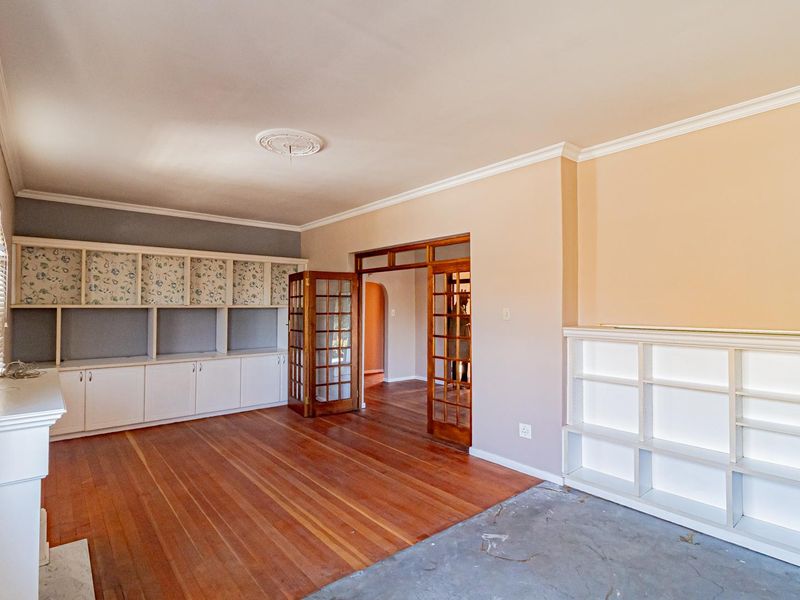 Spacious living room featuring hardwood floors, built-in cabinetry, and classic French doors, offering a versatile layout with potential for modern updates.