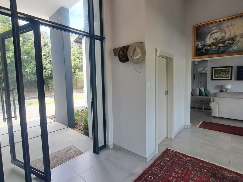 A bright and spacious entrance hall featuring high ceilings, large floor-to-ceiling glass doors, and neutral tiled flooring leading into the main living area.