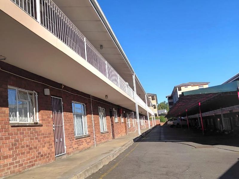 Exterior view of an apartment complex featuring a brick facade, upper-level balcony walkway, and a covered parking area.