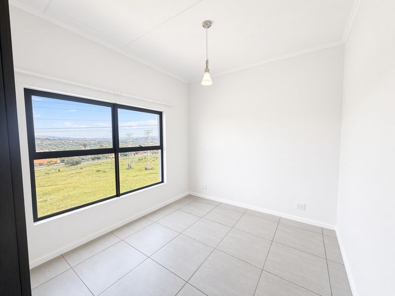 A bright, empty bedroom featuring neutral tiled flooring, a modern pendant light, and a large window offering expansive views.