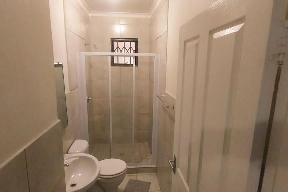 A compact bathroom featuring a glass-enclosed shower, pedestal basin, and toilet with neutral wall tiling.