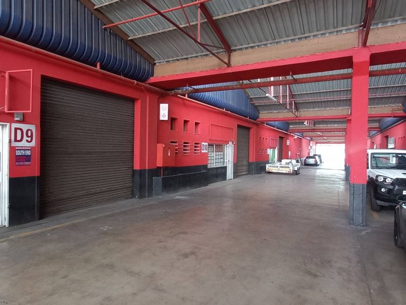 Spacious industrial utility area featuring concrete flooring, exposed steel roof trusses, and multiple roller shutter doors for efficient access.