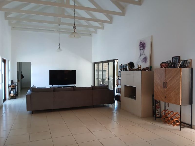 Spacious living room featuring a high vaulted ceiling with exposed rafters, tiled flooring, and a built-in fireplace, opening to an outdoor area.