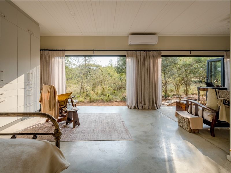 Spacious bedroom featuring polished concrete floors, extensive built-in cabinetry, and large sliding doors opening to a natural bushveld view.