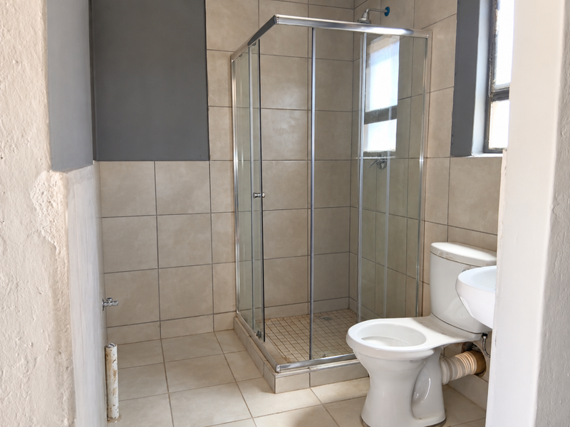 A functional bathroom featuring a glass shower enclosure, toilet, and washbasin, currently requiring cosmetic repairs to wall finishes and exposed plumbing.