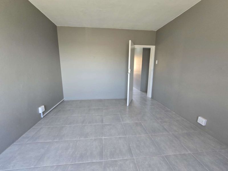 A clean, empty bedroom featuring neutral grey walls and modern tiled flooring, providing a versatile blank canvas for any interior design style.