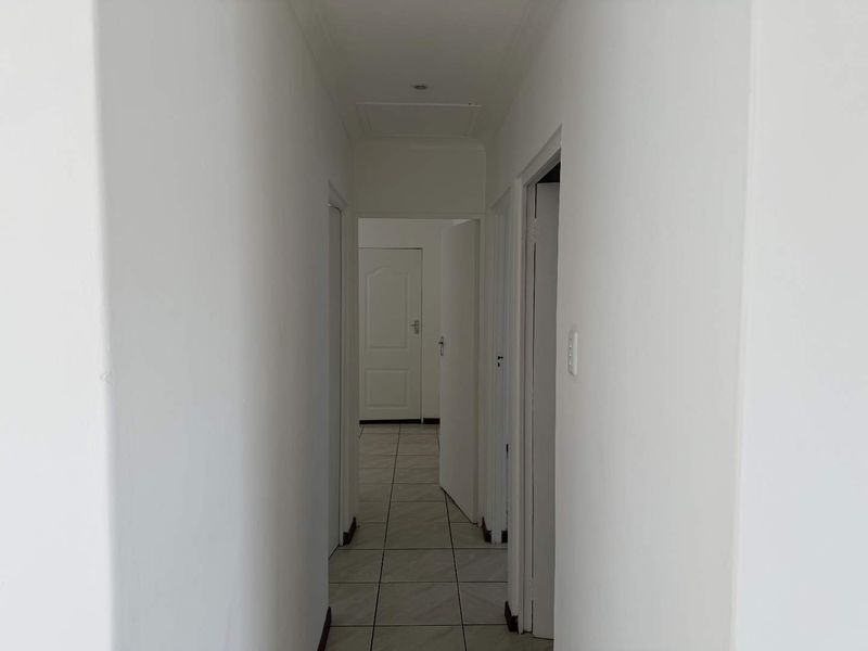 A clean, neutral hallway featuring tiled flooring and multiple internal door access points, providing a bright and functional transition space within the home.