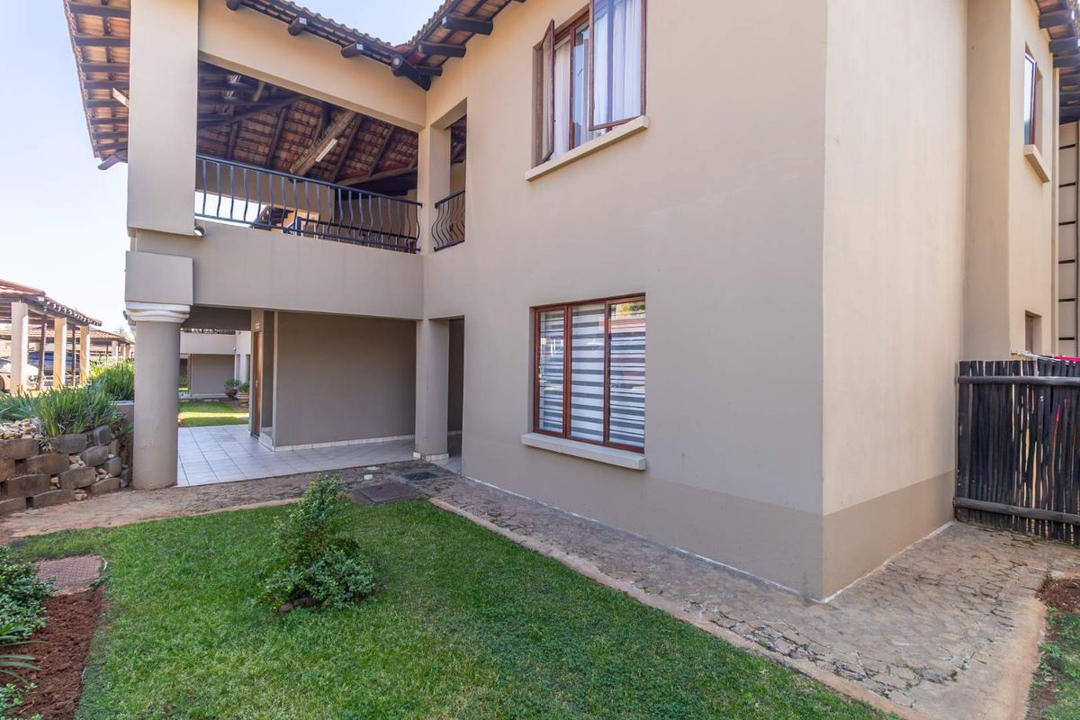 Rear view of the townhouse featuring a covered patio, upper-level balcony with wrought iron railings, and a small private garden area.