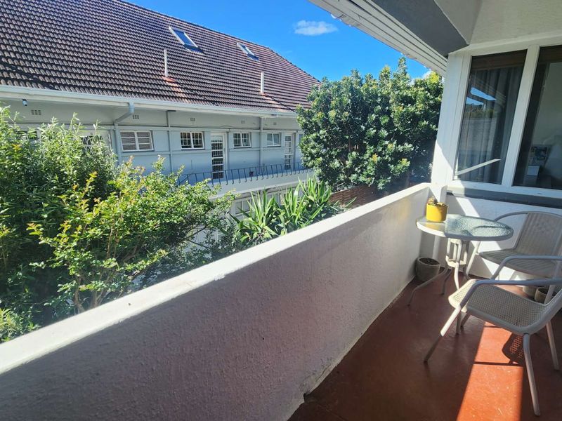 A private balcony featuring a solid masonry balustrade and direct access to the apartment via a sliding glass door, overlooking the complex grounds.